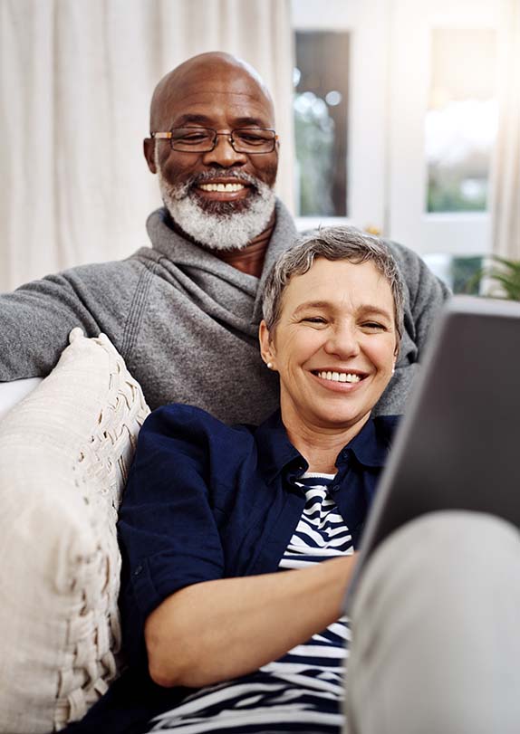 happy mature interracial couple in sofa using tablet