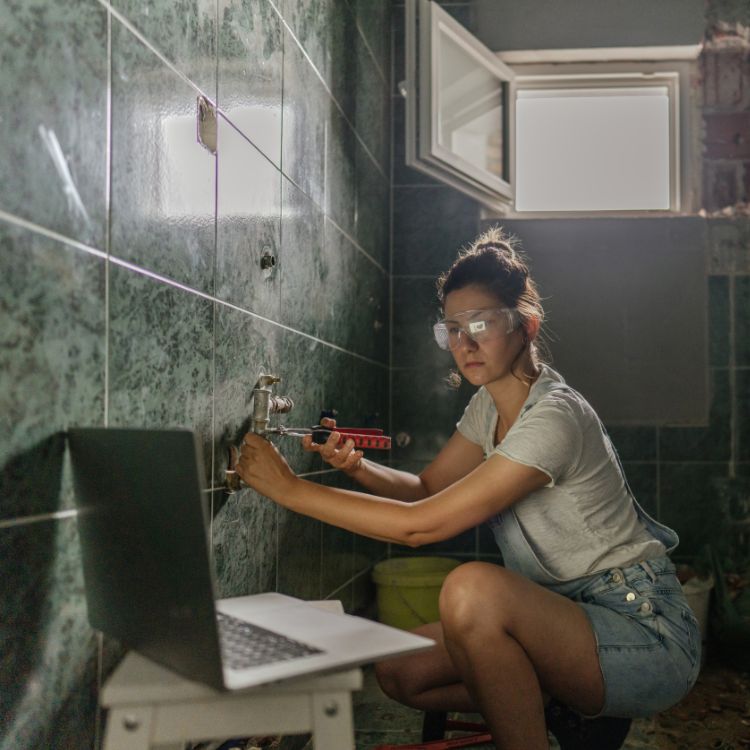 Persoon kijkt naar laptop voor uitleg tijdens het werken in de badkamer.